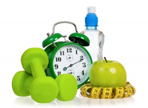 Green alarm clock, apple, bottle of water, measuring tape and dumbbells as concept of diet - isolated on white